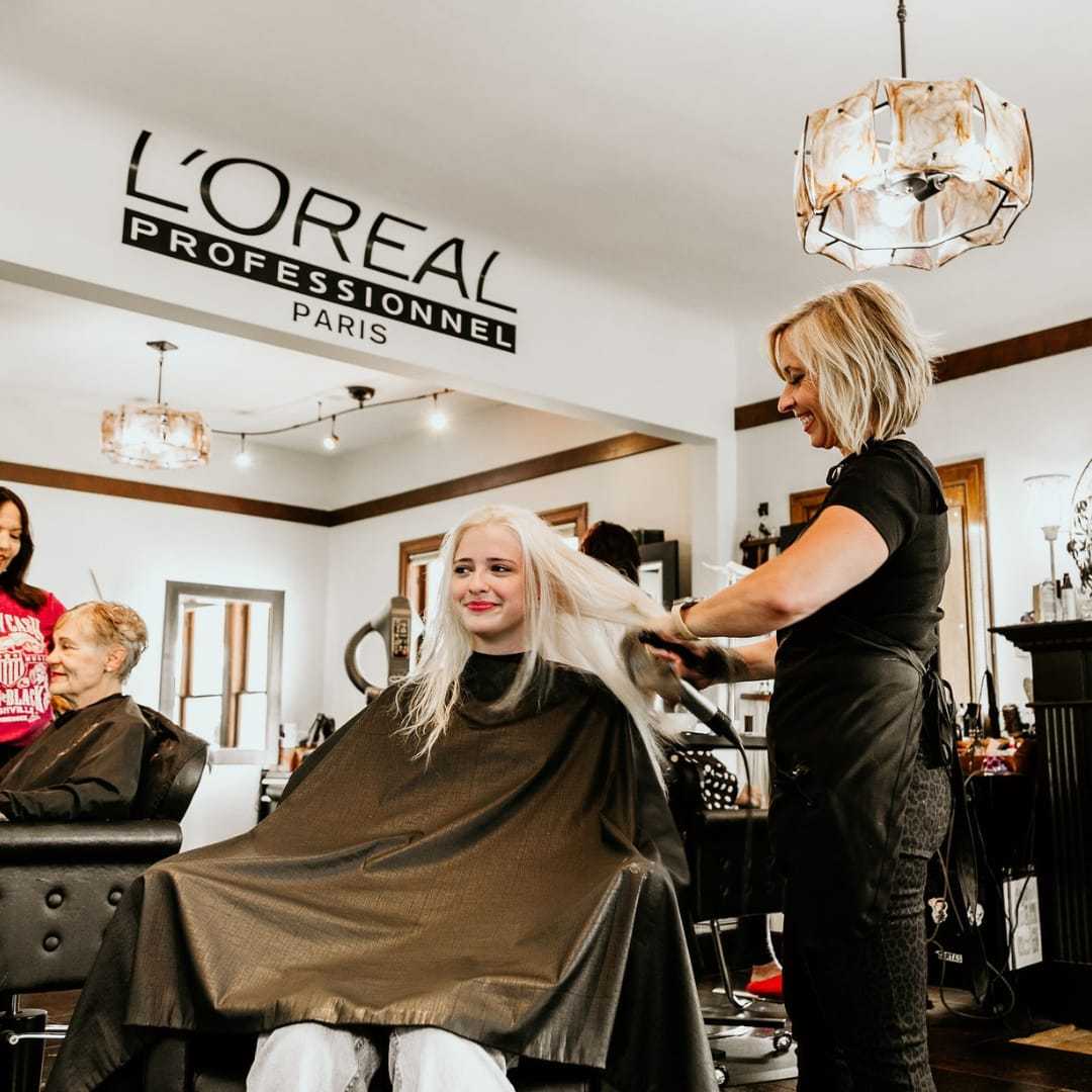 Hairdresser styling customer's long blonde hair in a salon.